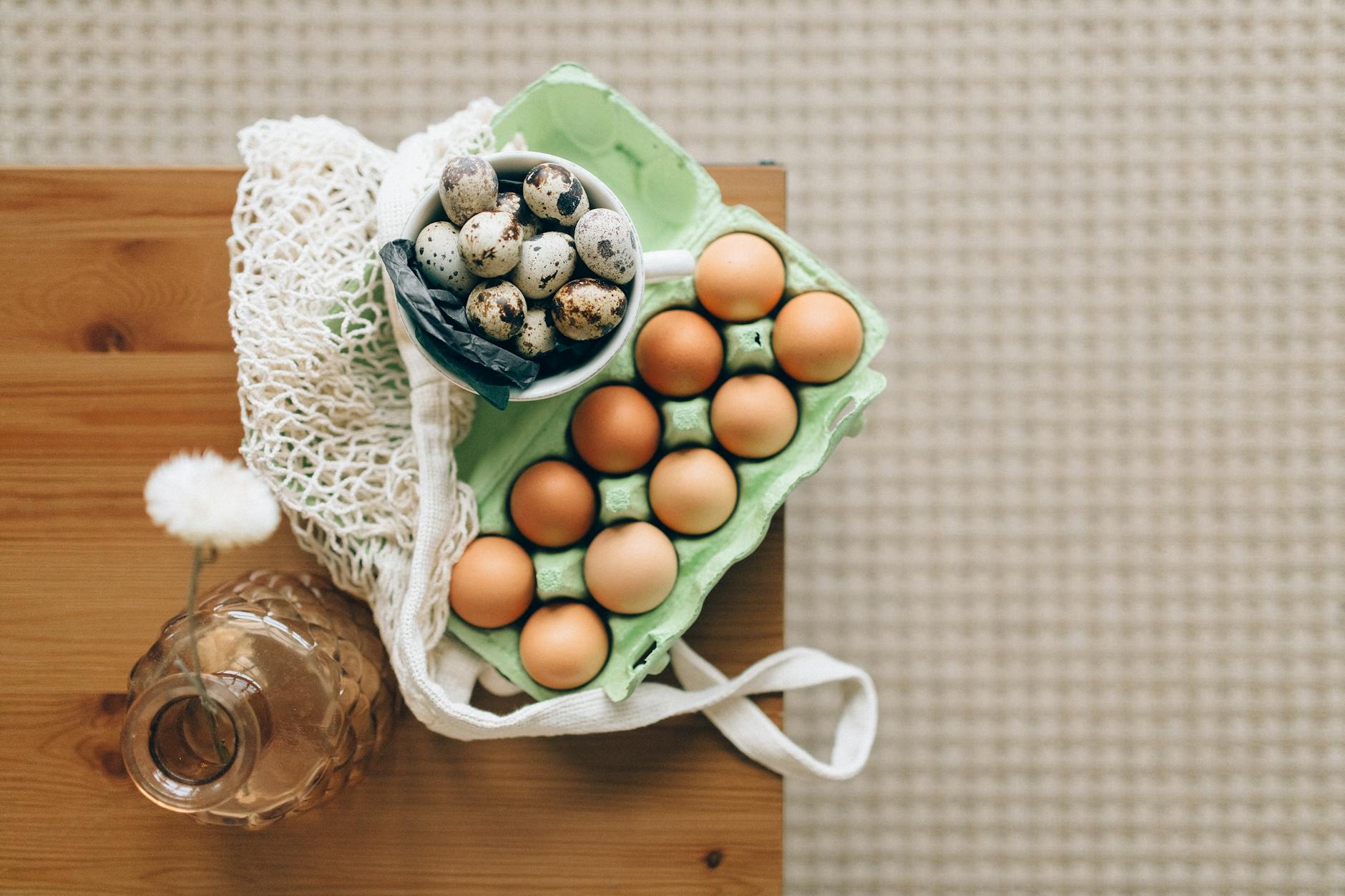 a bowl of quail eggs beside a tray of chicken eggs on a wooden table