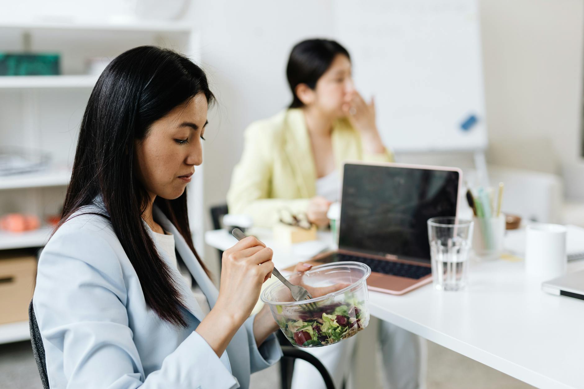 a woman in a blue blazer eating salad in the office